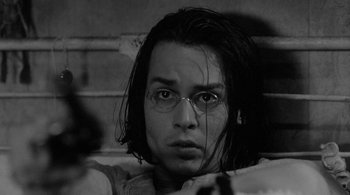 Movie still from “Dead Man” (1995), directed by Jim Jarmusch – A man with glasses is sitting in front of a brick wall; Close Up shot, High angle