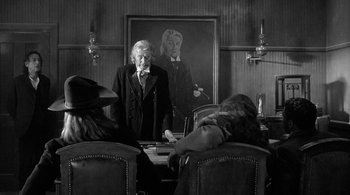 Movie still from “Dead Man” (1995), directed by Jim Jarmusch – An old man standing in front of a group of people in a room; Wide shot, Over the shoulder angle