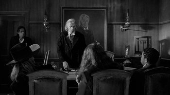 Movie still from “Dead Man” (1995), directed by Jim Jarmusch – Two people sitting at a table in front of a painting; Medium shot, Over the shoulder angle
