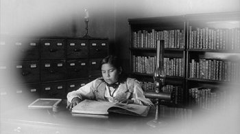 Movie still from “Dead Man” (1995), directed by Jim Jarmusch – A young girl sitting at a desk looking at a book; Medium shot, High angle