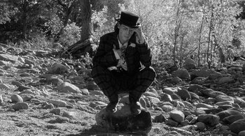 Movie still from “Dead Man” (1995), directed by Jim Jarmusch – A man squatting on a rock in the woods; Medium shot, High angle