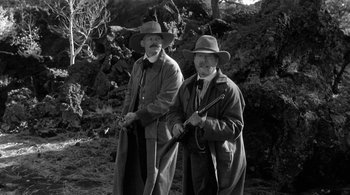 Movie still from “Dead Man” (1995), directed by Jim Jarmusch – A couple of men standing next to each other holding guns; Medium shot, Low angle