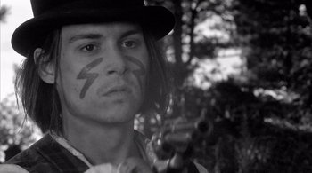 Movie still from “Dead Man” (1995), directed by Jim Jarmusch – A young man in a cowboy hat holding a gun in the woods; Close Up shot, Over the shoulder angle