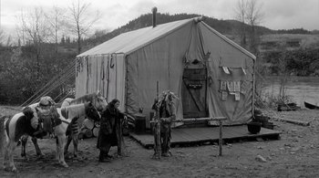 Movie still from “Dead Man” (1995), directed by Jim Jarmusch – A man standing next to two horses in front of a tent; Wide shot, High angle
