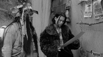 Movie still from “Dead Man” (1995), directed by Jim Jarmusch – A man in a fur coat holding a knife; Medium shot, Over the shoulder angle