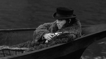 Movie still from “Dead Man” (1995), directed by Jim Jarmusch – A man in a fur coat and a top hat holding a gun; Medium shot, High angle