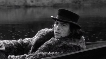Movie still from “Dead Man” (1995), directed by Jim Jarmusch – A man wearing a fur coat and a top hat in a boat on a river; Close Up shot, High angle