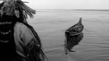 Movie still from “Dead Man” (1995), directed by Jim Jarmusch – A boat floating on top of a body of water near trees; Wide shot, High angle