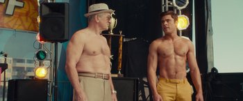 Movie still from “Dirty Grandpa” (2016), directed by Dan Mazer – Two men standing next to each other in front of a trophy; Medium shot, Over the shoulder angle