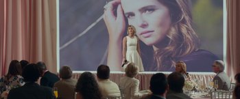 Movie still from “Dirty Grandpa” (2016), directed by Dan Mazer – A woman standing on a stage in front of an image of a woman; Wide shot, Over the shoulder angle