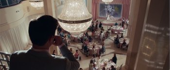 Movie still from “Dirty Grandpa” (2016), directed by Dan Mazer – A man in a suit is talking on a cell phone in front of a large chandelier; Wide shot, Over the shoulder angle