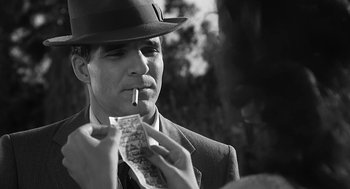Movie still from “Dead Men Don't Wear Plaid” (1982), directed by Carl Reiner – A black and white photo of a man smoking a cigarette and looking at a piece of paper; Close Up shot, Over the shoulder angle
