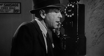 Movie still from “Dead Men Don't Wear Plaid” (1982), directed by Carl Reiner – A man wearing a suit and a hat smoking a cigarette in front of a phone; Close Up shot, Low angle