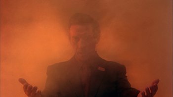 Movie still from “Death Race 2000” (1975), directed by Paul Bartel – A man in a suit and tie standing in front of an orange background; Medium shot, Low angle