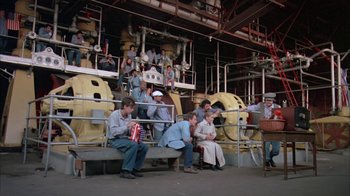 Movie still from “Death Race 2000” (1975), directed by Paul Bartel – A group of people sitting on a bench in front of a building; Wide shot, Low angle