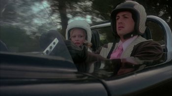 Movie still from “Death Race 2000” (1975), directed by Paul Bartel – A man driving a car with a child in the back seat; Medium shot, Over the shoulder angle