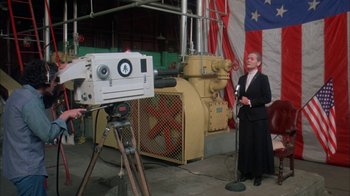 Movie still from “Death Race 2000” (1975), directed by Paul Bartel – A woman is standing in front of a video camera; Medium shot, Low angle