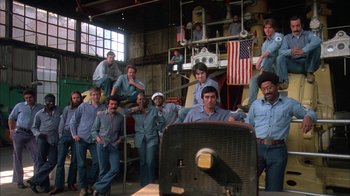 Movie still from “Death Race 2000” (1975), directed by Paul Bartel – A group of men standing next to an air conditioning unit; Wide shot, High angle
