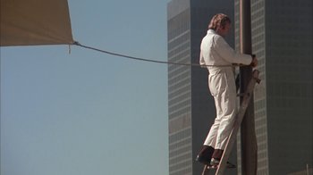 Movie still from “Death Race 2000” (1975), directed by Paul Bartel – A man on a ladder painting the side of a tall building; Wide shot, Low angle