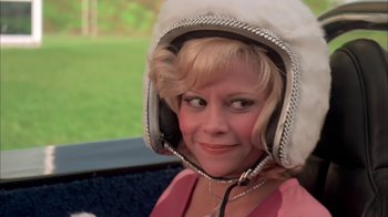 Movie still from “Death Race 2000” (1975), directed by Paul Bartel – A woman wearing a white hat and a pink dress; Close Up shot, Low angle