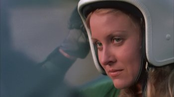 Movie still from “Death Race 2000” (1975), directed by Paul Bartel – A woman with a helmet on her head; Close Up shot, Low angle