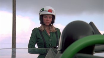 Movie still from “Death Race 2000” (1975), directed by Paul Bartel – A woman wearing a helmet standing in front of an airplane; Medium shot, Low angle