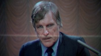 Movie still from “Death Race 2000” (1975), directed by Paul Bartel – An older man in a black suit and tie; Close Up shot, Over the shoulder angle