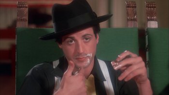 Movie still from “Death Race 2000” (1975), directed by Paul Bartel – A man in a hat is shaving his mustache; Close Up shot, Low angle