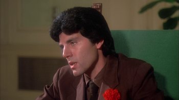 Movie still from “Death Race 2000” (1975), directed by Paul Bartel – A man in a brown jacket and a red flower in his hair; Close Up shot, Low angle