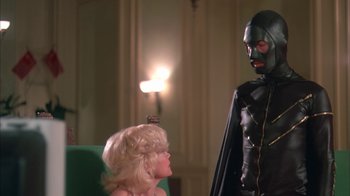 Movie still from “Death Race 2000” (1975), directed by Paul Bartel – A man in a black suit and a blonde wig; Medium shot, Low angle