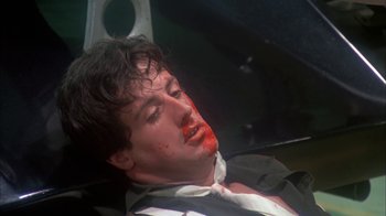 Movie still from “Death Race 2000” (1975), directed by Paul Bartel – A man with blood all over his face and neck; Close Up shot, Overhead angle