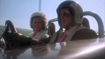 Movie still from “Death Race 2000” (1975), directed by Paul Bartel – A man and a woman driving a car in the road; Medium shot, Low angle