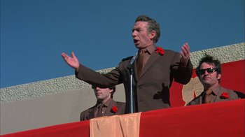 Movie still from “Death Race 2000” (1975), directed by Paul Bartel – A man in a brown suit is giving a speech to a crowd; Medium shot, Low angle