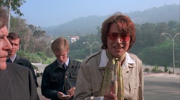 Movie still from “Death Race 2000” (1975), directed by Paul Bartel – A woman in a tan jacket and a man in a brown jacket are holding cellphones; Medium shot, Low angle