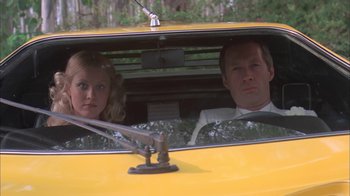 Movie still from “Death Race 2000” (1975), directed by Paul Bartel – A man and a woman sitting in the driver's seat of a yellow car; Medium shot, Low angle