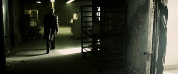Movie still from “Death Sentence” (2007), directed by James Wan – A person standing in a dark room next to a shelf; Wide shot, Over the shoulder angle