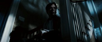 Movie still from “Death Sentence” (2007), directed by James Wan – A man standing on the stairs in the dark holding a book; Close Up shot, Low angle