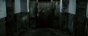 Movie still from “Death Sentence” (2007), directed by James Wan – A door to an empty room that is dark and dirty; Wide shot, High angle