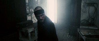 Movie still from “Death Sentence” (2007), directed by James Wan – A man with a bandage on his head is standing in a dark room; Medium shot, Low angle