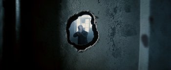 Movie still from “Death Sentence” (2007), directed by James Wan – A man taking a picture through a hole in a wall; Medium shot, Low angle