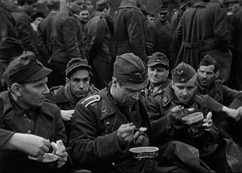 Movie still from “Decision Before Dawn” (1951), directed by Anatole Litvak – A black and white photo of a group of soldiers eating food; Medium shot, High angle
