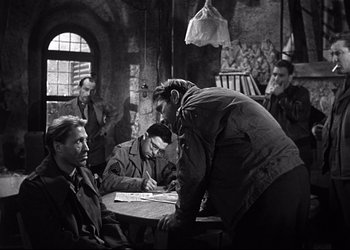 Movie still from “Decision Before Dawn” (1951), directed by Anatole Litvak – A group of men sitting around a table; Medium shot, Over the shoulder angle