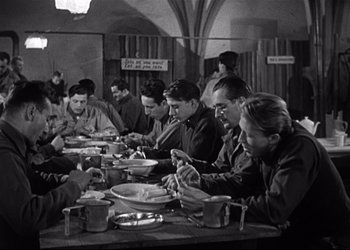 Movie still from “Decision Before Dawn” (1951), directed by Anatole Litvak – A black and white photo of a group of people eating; Wide shot, High angle