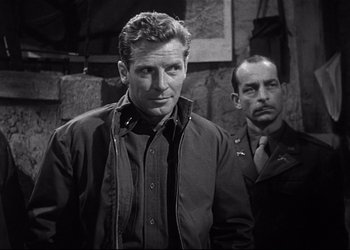 Movie still from “Decision Before Dawn” (1951), directed by Anatole Litvak – A man standing next to another man wearing a jacket; Medium shot, Over the shoulder angle
