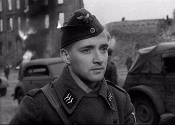 Movie still from “Decision Before Dawn” (1951), directed by Anatole Litvak – A man in a military uniform standing in front of a building; Close Up shot, Low angle