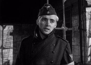 Movie still from “Decision Before Dawn” (1951), directed by Anatole Litvak – A man in a military uniform is standing in front of a brick wall; Close Up shot, Low angle