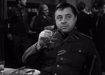 Movie still from “Decision Before Dawn” (1951), directed by Anatole Litvak – A man in military uniform holding a glass of wine; Close Up shot, Over the shoulder angle
