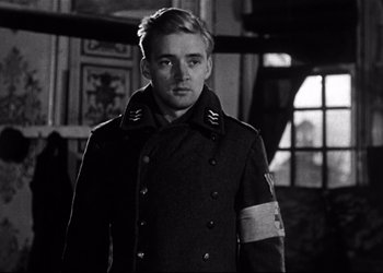 Movie still from “Decision Before Dawn” (1951), directed by Anatole Litvak – Black and white photograph of a young man in a military uniform; Medium shot, Over the shoulder angle