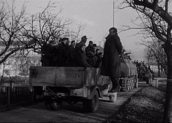 Movie still from “Decision Before Dawn” (1951), directed by Anatole Litvak – A group of people riding in the back of a truck down a street; Wide shot, Low angle
