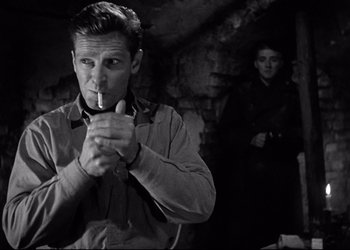 Movie still from “Decision Before Dawn” (1951), directed by Anatole Litvak – A black and white photo of a man smoking a pipe; Medium shot, Low angle